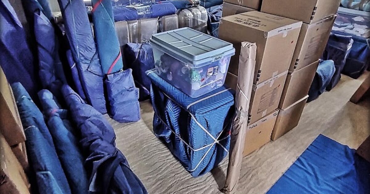 Furniture wrapped in blue moving pads beside packed boxes and floor protection