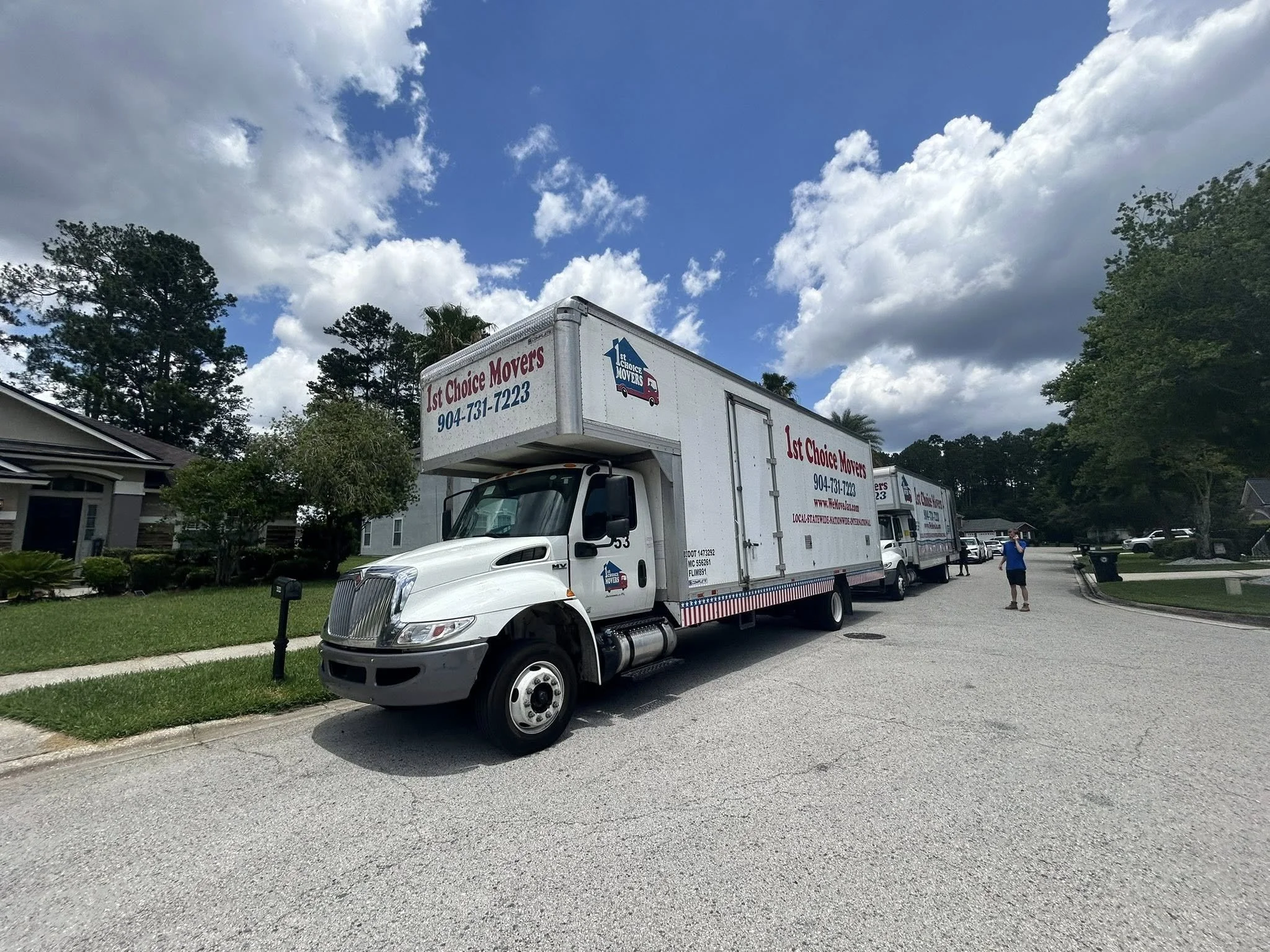 Two 1st Choice Movers trucks on a residential street under a blue sky