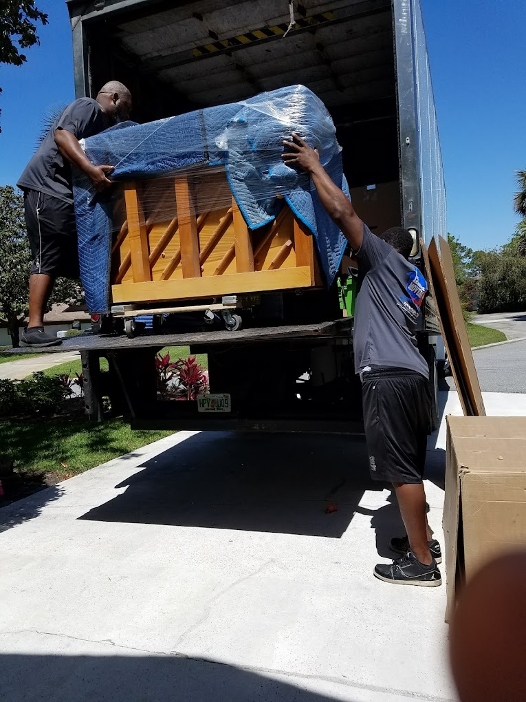 Moving crew loading a wrapped upright piano onto a truck